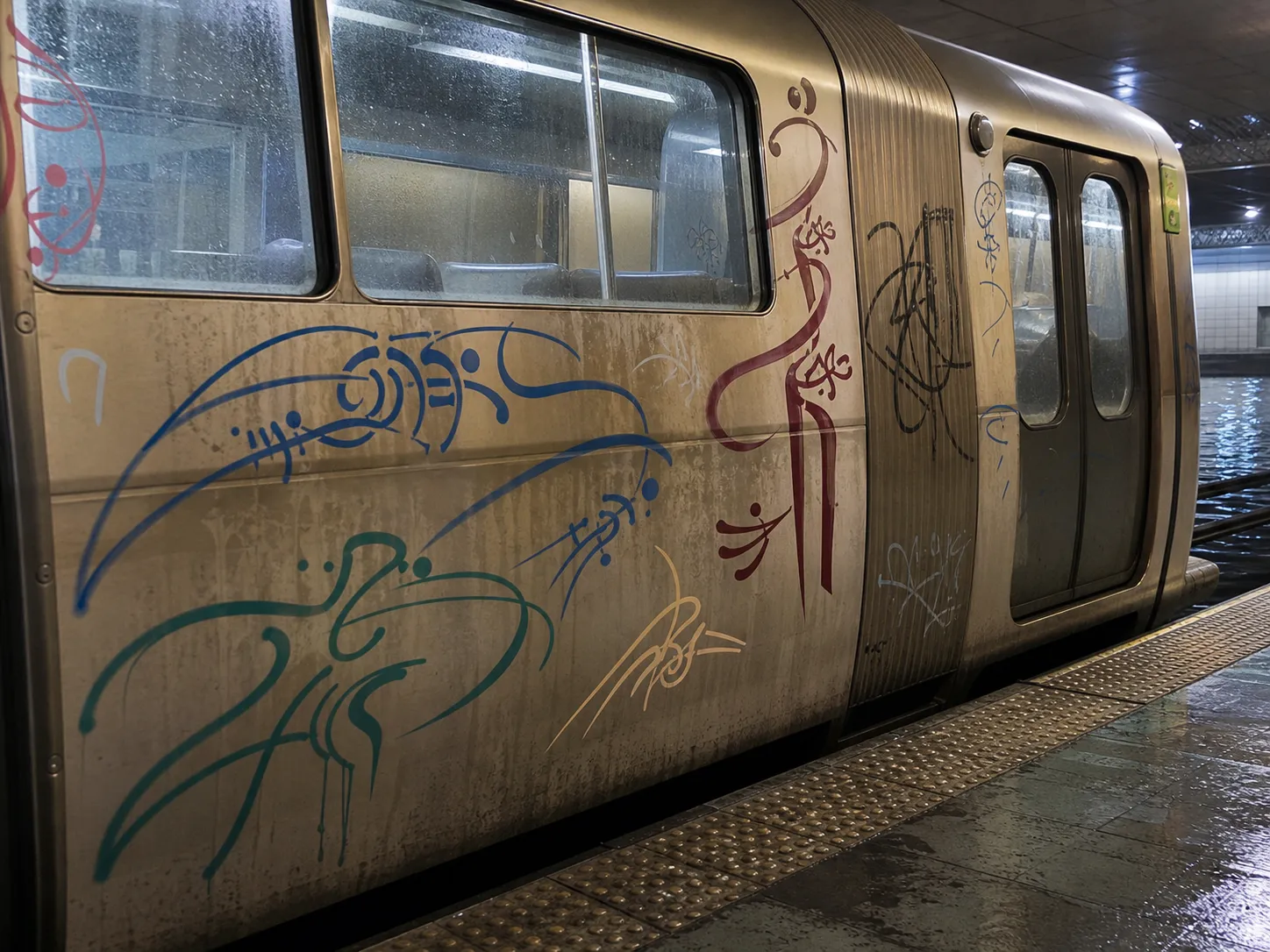 A damp New Atlantis shell-car train photographed at a station, its side marked with blue, teal, red, black, and pale shell-script tags.